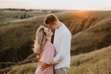 Beautiful woman and man are hugging and kissing on the field at sunset. A young couple hugging and kissing on a field at sunset.
