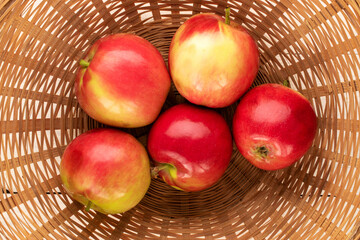 Several juicy red apples in a straw basket, macro, top view.