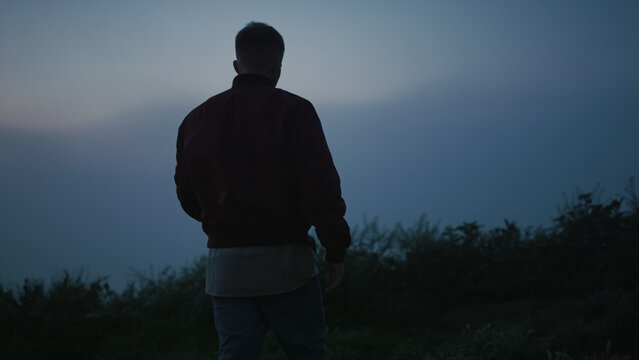 Back view young guy walking in field at morning. Casual man hiking in mountains