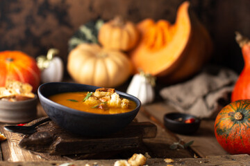 Hot pumpkin soup in ceramic plate with ripe pumpkins,bread croutons garnished with fresh sage...