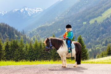 Kids riding pony. Child on horse in Alps mountains