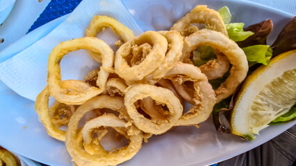 A plate full of fried squid rings with fresh lemon served in a local restaurant in coastal village of Los Abrigos, Tenerife, Canary Islands, Spain, Europe, EU. Local traditional food. Sea fruit food