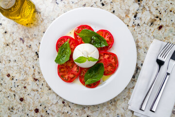 Salad with buratta cheese and tomatoes with basil on white plate on marble table top view