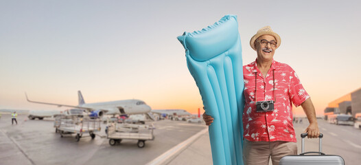 Happy mature male tourist holding a inflatable mattress and a swimming ring on an airport