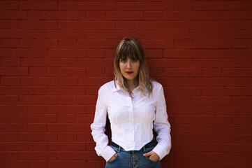 Pretty, blonde, young woman having fun making different expressions in front of a red background wall. Concept various expressions. Laughter, sadness, tired, angry, hate.