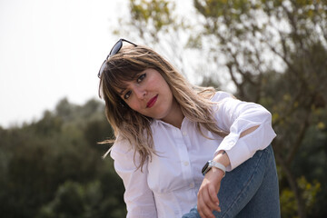 Beautiful, blonde, young woman is sitting on a bench doing different poses and expressions. The woman is on holiday in the city. Travel and holiday concept.