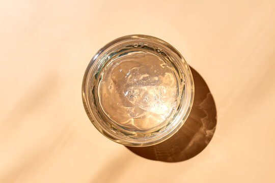 Jar with transparent cosmetic product, gel or cream on beige colored background. Unbranded package with of antioxidant cream for self-care. View from above.