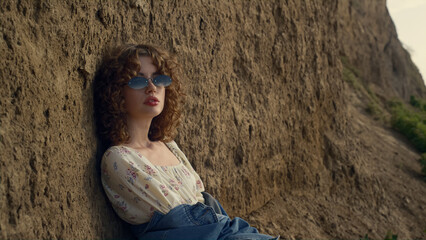 Relaxed woman sitting beach leaning on hill close up. Girl in sunglasses posing.