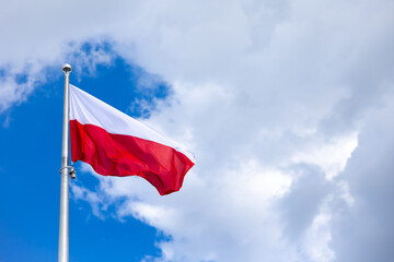 National banner of Poland wave in the background of blue sky with little small clouds. Picture taken in midlle of the day.