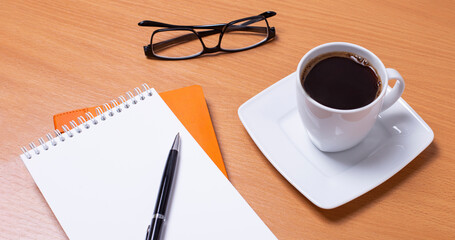 Side view of an office desk. Workspace with empty board, black framed glasses, pen and coffee cup on wooden background.
