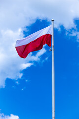 National banner of Poland wave in the background of blue sky with little small clouds. Picture taken in midlle of the day.