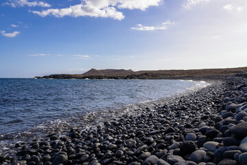 Panoramic view on black stone pebble beach Playa Colmenares near Amarilla, Golf del Sur, Tenerife, Canary Islands, Spain, Europe. Montana Amarilla in the back. Tranquil waves from the Atlantic Ocean