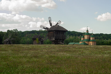 Fototapeta na wymiar Old windmill and a wooden church in the field. 