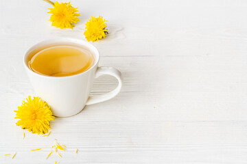 Cup of healing herbal tea with yellow dandelions blossoms and leaves