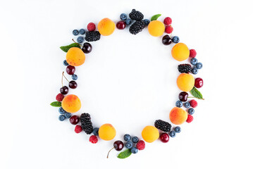 On a white background, fruits are laid out in a circle: apricots, cherries, blackberries, raspberries, blueberries, mint leaves.