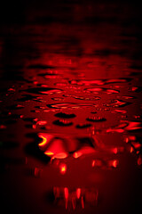 Beautiful macro photo of water drop reflection, lying on surface, front view. Close up of red liquid with side lighting from displays.