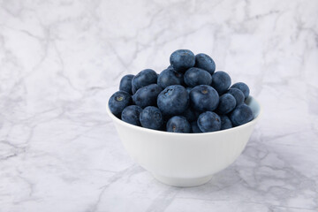 Blueberries in a bowl on a white marble background. Ripe and fresh blueberries. Vitamins. Healthy food. Juicy berry. Copy space. Place for text