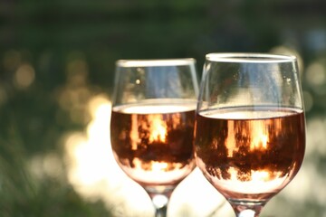 Glasses of tasty rose wine on blurred background, closeup and space for text. Picnic season
