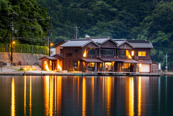 Fototapeta premium Lights from waterside restaurant reflect off water in early evening at Ine