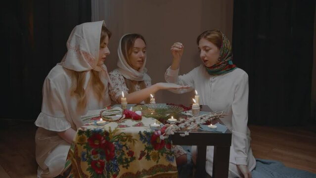 4K. Slavic women are guessing with a ring in a dark room by candlelight