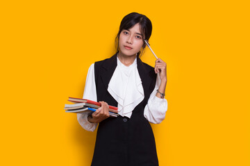 beautiful asian woman hug a book and thinking idea isolated on yellow background
