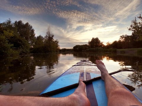 Man sitting on sup board on river in nature at sunset. POV