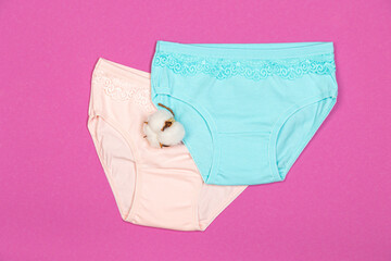 Clothes for children in the form of panties on a pink background. Clothes for children from soft fabric. Panties for girls and cotton flower top view flat lay with copy space for text.