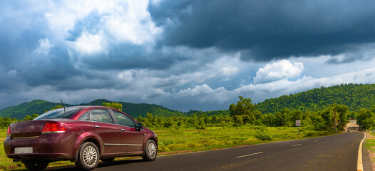 A Red Sedan Parking on the Roadside Overlooking Mountains with moody skies . Selective Focus is used. 