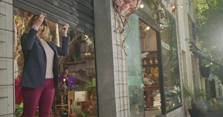 Businesswoman owner of small business store at sidewalk level opening storefront sliding shutters up. Open for business concept. Female entrepreneur opened for customers and clients