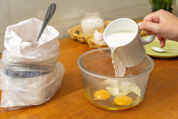 Making pancakes, cake, baking side view of baker hands pouring batter and whisking batter in bowl. Concept of Cooking ingredients and method. Milk is poured into a deep bowl with eggs.