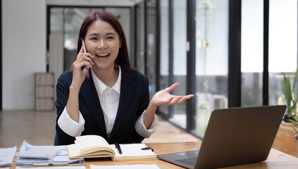 Charming Asian woman with a smile standing holding papers and mobile phone at the office.