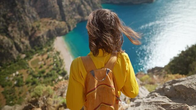 aerial top view woman traveler with blowing hair enjoying beautiful view of Butterfly Valley from edge of cliff on mountain top, Butterfly Valley in city of Oludeniz, Fethiye in western Turkey
