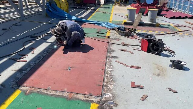 View of the deck of the ship, which is standing near the shore during repairs. The welder is doing the job.