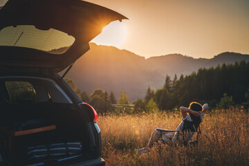 Young beautiful woman traveler enjoying the sunset in the mountains while traveling by car - Powered by Adobe