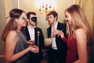 People in masquerade masks eating melon during party