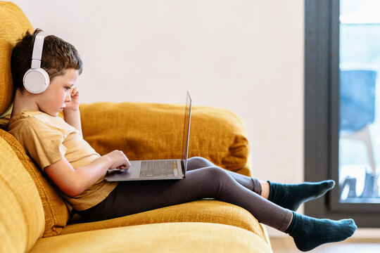 Boy sitting on a sofa with headphones on his head and using the laptop