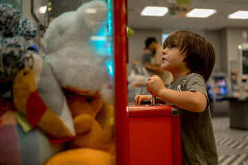 Children are standing near a machine with soft toys and playing, they want to catch and pull out a...