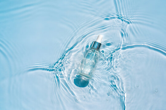 Serum, essence with collagen in transparent bottle with a pipette on water blue background