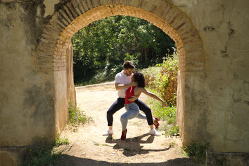 Obraz na płótnie Canvas Attractive young couple dancing sensual bachata under an ancient stone arch in an outdoor park. Latin, sensual, folkloric, urban dance concept.