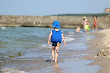 Mały chłopiec biegnie po piaszczystej plaży nad wodą.