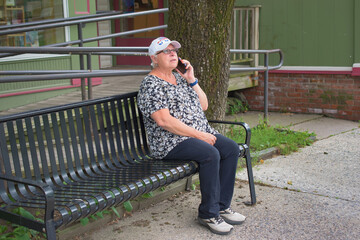 A mature woman is sitting on the wrought iron bench in Woodstock NY making a phone call on her cell...