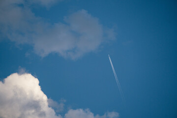 Naklejka na ściany i meble Plane crossing the blue sky and leaving a trail in its wake.