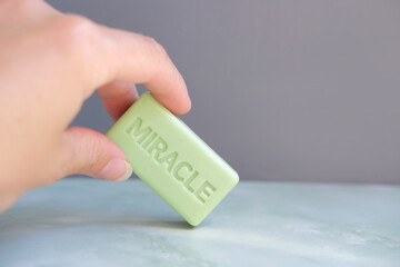 Hand holding a small green soap with inscription miracle close up