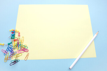 blank yellow sheet with pencil multicolored buttons and paper clips on blue background