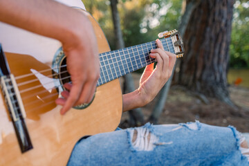 Guitarist plays the guitar. Professional guitarist plays guitar outdoors. Musician plays a classical guitar in the park. Close-up of the musician's playing hands.