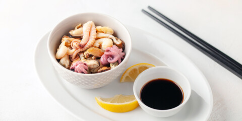 Mix of sea food - mussels, squid, octopus, shrimp in a bowl, lemon and soy sauce. Top view.