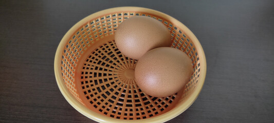 Hard-boiled chicken eggs in an orange plastic basket. resting on black wooden floor - top