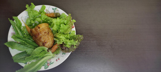 Baked chicken breast fillet with lettuce in a plate on a black table Leave a blank space for text on the right.