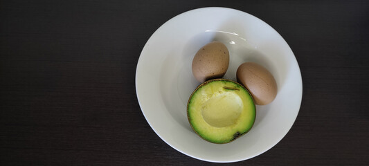Boiled Eggs and Avocado in a white plate placed on a black wooden table top view