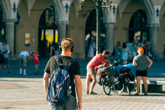 A young man in a T-shirt with a travel backpack on his back and headphones on his head travels through the old town in front of a man and a woman traveling on bicycles, a sunny day in Krakow